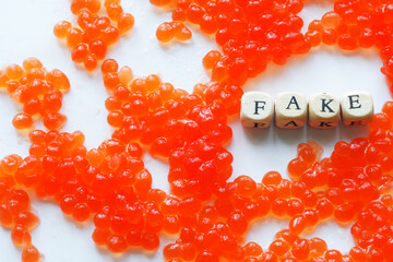 Artificial fake red caviar on a white surface next to the fake sign. The concept of unnatural food,...