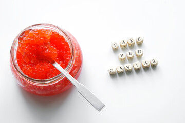 Glass jar of artificial fake red caviar stands next to the fake red caviar sign. White background....