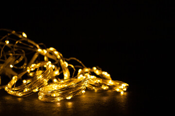 Christmas decor. Illumination for the New Year. Glowing garland on a black background. Festive background. Christmas background. Golden threads. Postcard in luxury style.