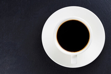 Cup of black coffee on a white saucer. Morning coffee in ceramic cup on a dark background. Top view. Copy space