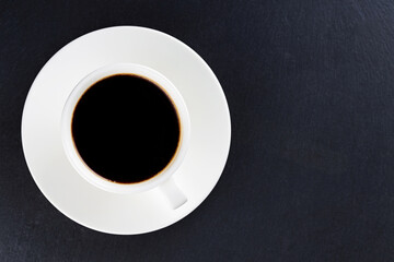 Cup of black coffee on a white saucer. Morning coffee in ceramic cup on a dark background. Top view. Copy space