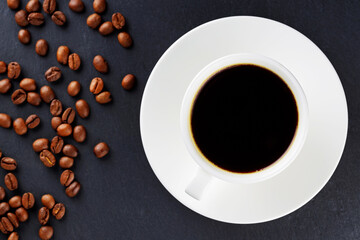 Cup of coffee on a saucer and roasted coffee beans. Black coffee in ceramic cup on a dark background. Food background. Top view. Copy space