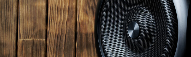 Single-way mid-range or low-frequency speaker system with a metal grill and an imitation of a tweeter speaker set against a background of natural pine boards. Eco-style. Web banner