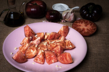 Tomato of the Mar Azul variety, chopped and dressed for salad, accompanied by garlic, salt flakes, pepper, oil and whole tomatoes.