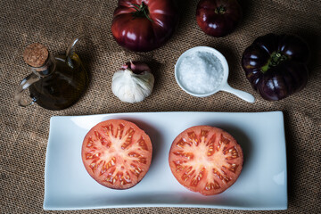 Tomato of the Mar Azul variety, split in half and presented on a plate, with the ingredients for its dressing.