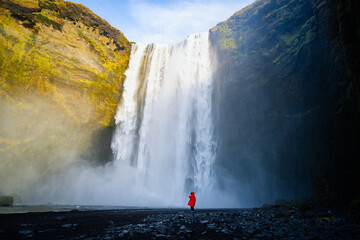 A person admirnig the beauty of Skogafoss waterfall located in Iceland. Girl tourist enjoying freedom on vacation at waterfall