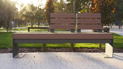Modern wooden benches on the lawn in the park. Stylish new bench in city recreation area on sunrise or sunset. Urbanism theme public space landscape design. No people on empty street sidewalk.
