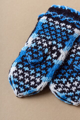 Knitted mittens on beige background. Warm handmade mittens for winter. Dark blue and black pattern. Back side