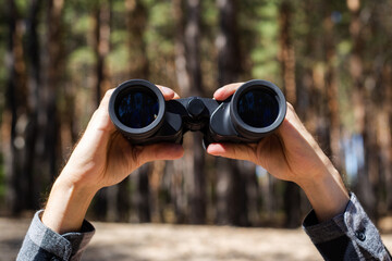 Man holds binoculars against the background of the forest
