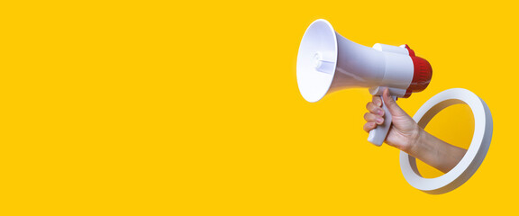 Female hand holds a megaphone in a round hole on a yellow background. Banner. - obrazy, fototapety, plakaty