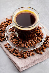 Americano coffee and roasted coffee beans on a gray background. Morning coffee in glass cup on a linen napkin