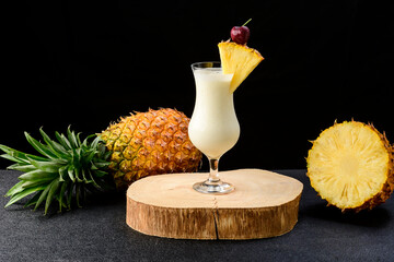 two glasses with pina colada cocktail, a whole pineapple next to the drinks, isolated on black...