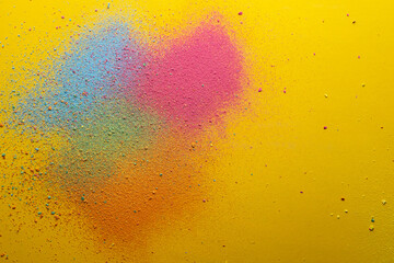 Multicolored, bright powder scattered on a yellow background. Copy space. Abstract texture. Top view. 