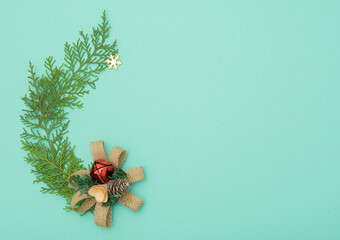 Christmas decoration on a green coniferous branch on a mint green background. Red bell. Abstract image of a festive background for the design of postcards with a place for text
