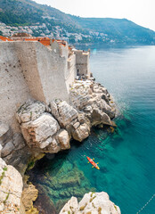 View from the rock cliffs of kayaker exploring the crystal clear Mediterranean waters of a cove off...