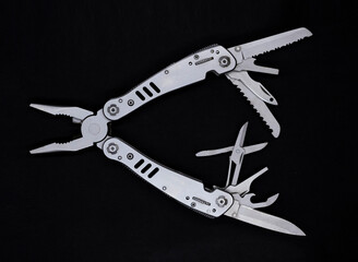 multitool in gray color on a black background. multifunctional universal hand tool