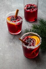Hot mulled wine for winter with cranberry, spices, cinnamon and orange slices in glass cup and bottle on grey table. Christmas drink. Festive concept with Christmas tree branches. Selective focus.