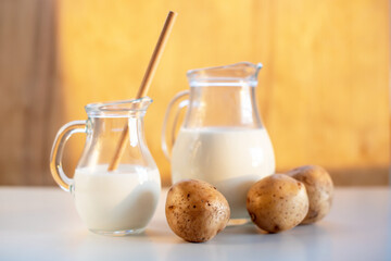 Vegan plant milk from potato in glass jar and potato tubers on the table. Concept of potato milk, vegan sustainable option, plant-based dairy. Substitute drink, healthy eating, diet, nutrition