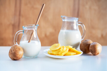 Vegan plant milk from potato in glass jar and potato tubers on the table. Concept of potato milk, vegan sustainable option, plant-based dairy. Substitute drink, healthy eating, diet, nutrition