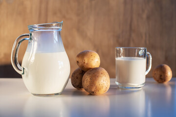 Vegan plant milk from potato in glass jar and potato tubers on the table. Concept of potato milk, vegan sustainable option, plant-based dairy. Substitute drink, healthy eating, diet, nutrition