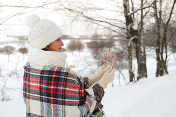 A woman walks through the winter forest, she holds candy canes in her hands.