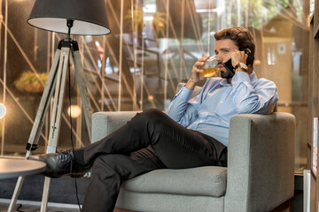 Attractive entrepreneur having a phone call in his office with a drink