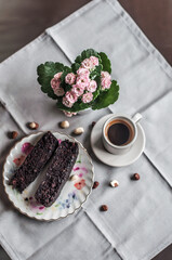 Chocolate cake on a plate with pattern, a cup of coffee and Kalanchoe.
