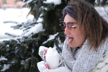 Portrait of a girl on the background of a Christmas tree. She holds a mug with snow in her hands.