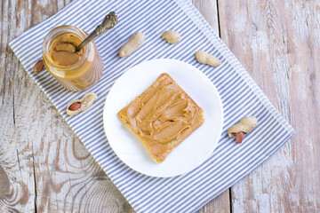 Peanut butter in a glass jar with a napkin on a wooden background. Delicious and healthy breakfast.