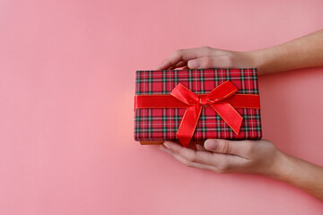 girl's hands are holding gift box tied with red ribbon with bow on pink background. Gifts for holiday. Valentine's day. Copy space