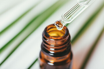 Pipette drips essential oil into bottle against background