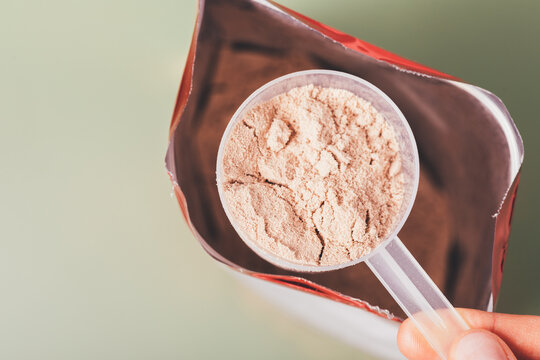Close-up whey protein measuring spoon over open package bag