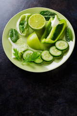 Organic green vegetables and fruits on a dark background. Green diet food on a plate. Healthy food. Top view. Copy space