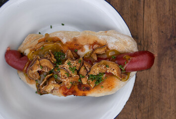 Fast food. Closeup view of a gourmet hot dog with fried sweet potato chips, mozzarella cheese and mustard, in a white bowl on the wooden table.