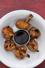 Top view of deep fried breaded chicken wings with a bittersweet dipping sauce, in a white bowl on the red wooden table.
