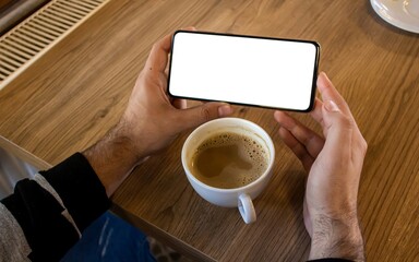 Fototapeta na wymiar Hand holding mobile phone with blank white screen while drinking coffee.