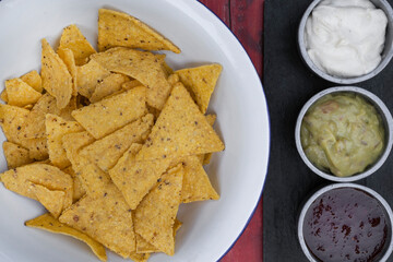 Mexican food. Top view of nachos in a white bowl and three dipping sauces of cheddar cheese, sweet chili and guacamole.