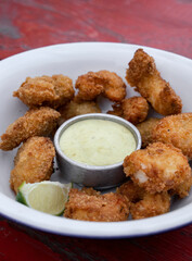Closeup view on fried breaded shrimps with avocado mayonnaise and lemon in a white bowl. 