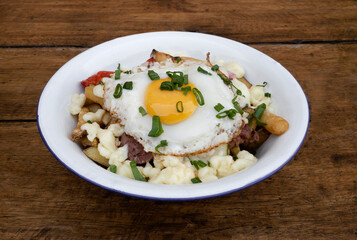 Closeup view of fried potatoes with melted cheese, chorizo, bell pepper, onion and a grilled egg in a white dish.