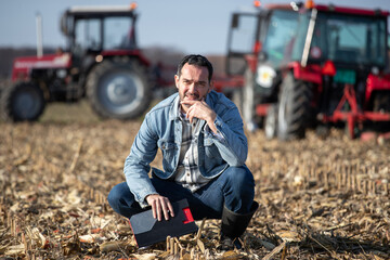 Farmer squatting in field with tractors in background