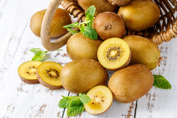 Ripe raw kiwi gold whole and slices falling from basket with mint leaves