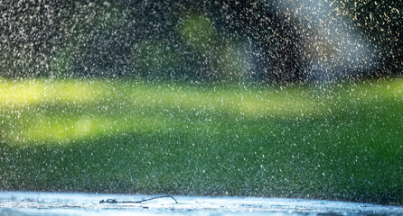 Raindrops fall on the asphalt and green grass.