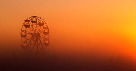 Big white Ferris wheel in a foggy park at dawn.