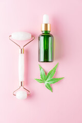 Herbal extract and cannabis leaf in green transparent bottle dropper. Rose quartz face massage roller, Concept for natural eco cosmetics.