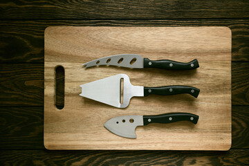 Three-piece cheese knife set lies on a wooden cutting board