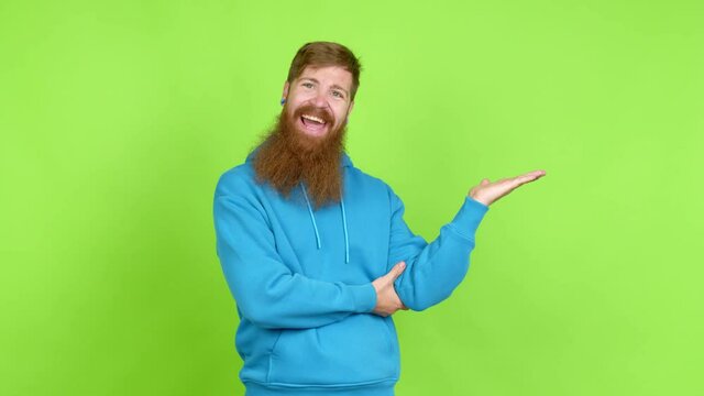 Redhead man with long beard extending hands to the side and inviting to come over isolated background