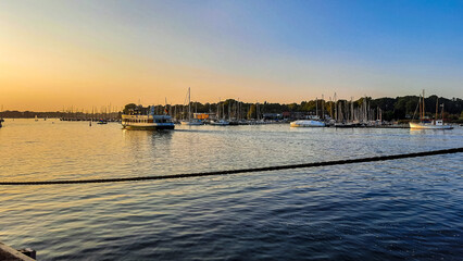 Orange-blauer Himmelübergang am Wasser mit malerischem verträumten Hafen und kleinen Schiffen mit...