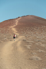 Fototapeta na wymiar Mujer caminando por un sendero para subir una colina con una paisaje volcánico, rocoso y desértico. (La graciosa, Islas Canarias, España)