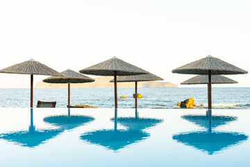 Deck chairs under sun umbrella between an infinity pool and the sea. Copy space provided on top.