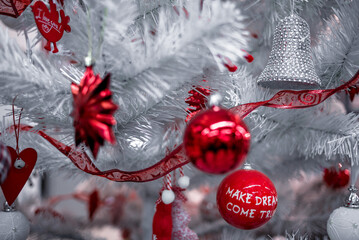 Beautiful Christmas red and silver balls on a white Christmas tree with decorations in the form of ribbons with the inscriptions Merry Christmas and Happy New Year
